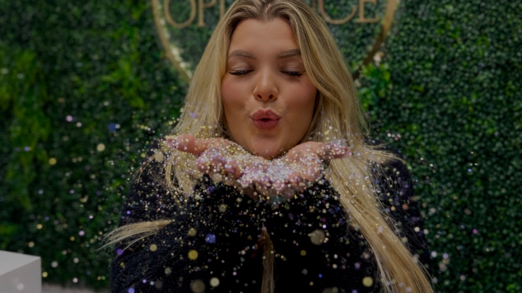 Brandi, founder of Opulence Beauty, blowing glitter at her Cornelius studio front desk
